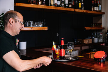 Mature and experienced waiter taking an order at the bar counter with a tray. Worker in his small business - Powered by Adobe