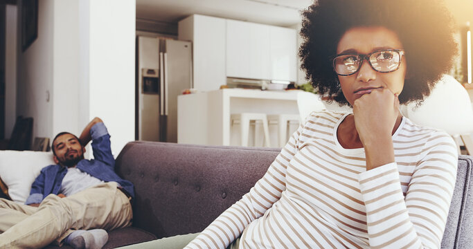 He Can Annoy Me So Much Sometimes. Shot Of A Annoyed Looking Woman Seated On A Couch Resting With Her Chin On Her Fist While Ignoring Her Boyfriend At Home.