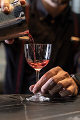 the bartender pours a red drink into a glass on the bar counter