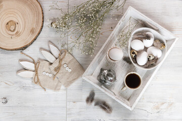 Table decorated for Easter in beige tones. Dried gypsophila, chicken and quail eggs, a silver figurine of a hare and a cup of coffee. Easter concept.