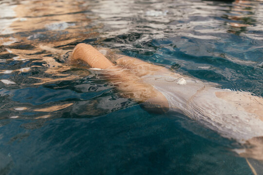 woman body in pool with sparkle dress on swimming on back