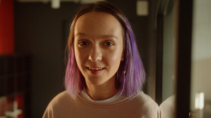 A young girl-student standing near the window, looking at the camera and smiling