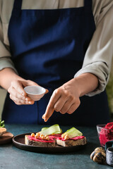 Woman making tasty sandwich with healthy hummus at table