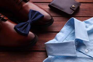 Men's fashion. Men's shoes, bow tie, shirt, and wallet on wooden table. Selective focus