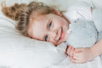 Little cute girl with curly hair sleeps in bed on a white bed with her plush toy. Healthy sleep. The child is resting.