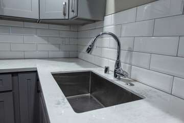 Angled view of a white, empty kitchen with marble countertops and a gas stove, the faucet in view in the background