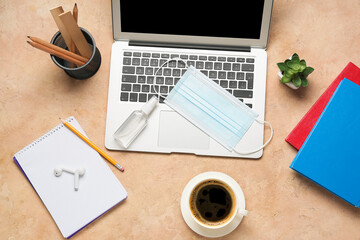 Modern laptop, earphones, medical mask, antiseptic and cup of coffee on color background