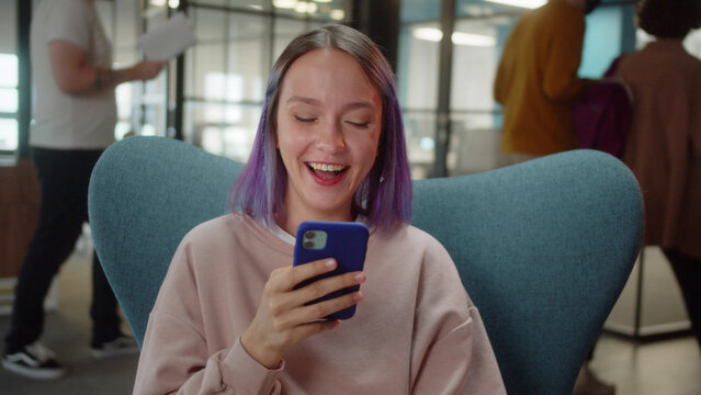 A young cute student sits on the chair and reads humorous posts on the Internet, close up slow motion