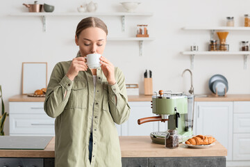 Young woman drinking tasty coffee in kitchen