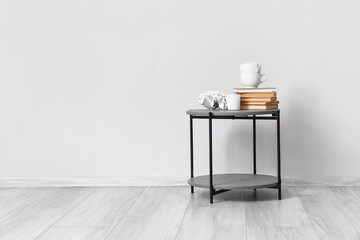 Small table with cups, books and decor near light wall