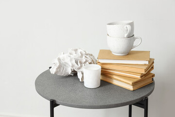 Small table with cups, books and decor near light wall