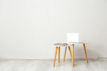 Small tables with laptop and magazines near light wall