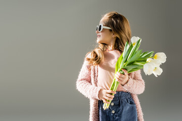 happy kid in sunglasses holding flowers isolated on grey.