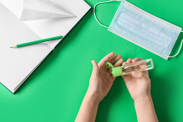Child's hands with bottle of sanitizer, medical mask and book on green background