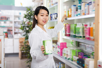 Focused Chinese pharmacist is searching medicines on shelves in drugstore