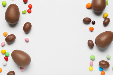 Delicious chocolate eggs and candies on light background