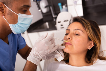 Young Hispanic woman getting procedure of injection contouring for facial correction in aesthetic cosmetology clinic