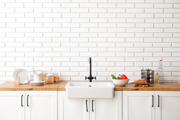Counters with sink, food and kitchen utensils near white brick wall