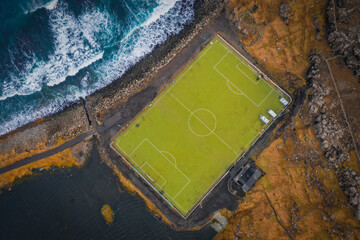 Aerial view of an old football field with scenic cliffs in the background located on the coast near the village of Eidi in Faroe Islands, Denmark. November 2021 © Сергій Вовк