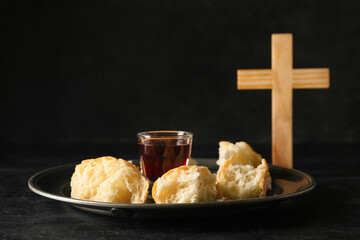 Tray with glass of wine, bread and cross on dark background