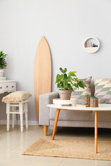 Interior of light living room with wooden surfboard, tables and sofa