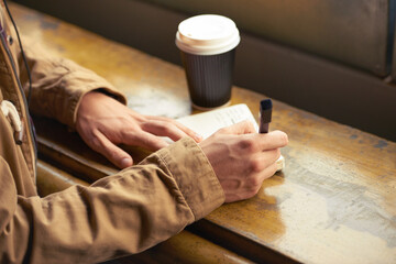 Fototapeta na wymiar I wrote a letter to my love. Closeup shot of a man writing in a notebook while sitting in a cafe.