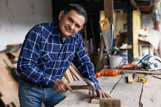 Hispanic carpenter nailing into wood - worker man with carpentry tools - man hammering