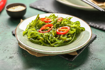 Plate with healthy seaweed salad and chili pepper on green background