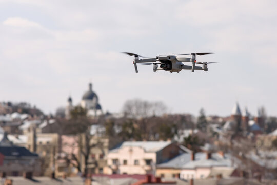 A modern quadcopter with a high resolution camera hovering in the air. A compact gray RC drone takes aerial photo or video footage from the air. Gadget in flight over the city. Drone control.