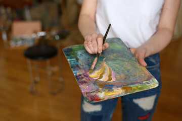 Wooden palette close-up. The artist girl mixes various shades of bright colored oil or gouache...