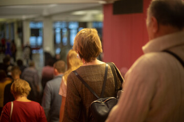 People are walking inside building. Lot of people leave room. Old people after concert.