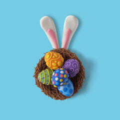 Happy Easter flat lay style composition. Nest with eggs and rabbit ears made of plasticine on a blue background with copy space. Top view - obrazy, fototapety, plakaty