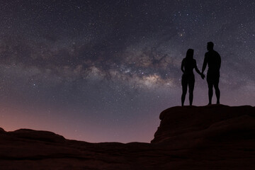 Milky Way with silhouette of people. Landscape with night starry sky. Standing man and woman on the mountain with yellow light. Beautiful galaxy. Universe.