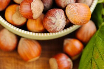 Hazelnuts close-up in a green cup on a wooden table. Whole nuts with green leaves. Fresh harvest of hazelnuts. Farmed organic ripe hazelnuts