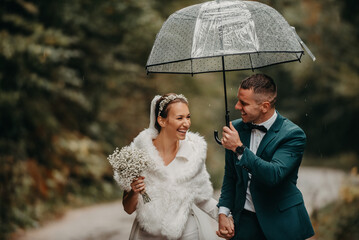 Wedding happy moments. Happy young couple, newlyweds walking the streets in rainy weather while carrying an umbrella.