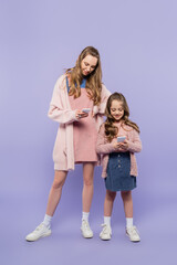 full length of mother and daughter using gadgets on purple.