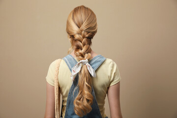 Young woman with stylish bandana on beige background, back view