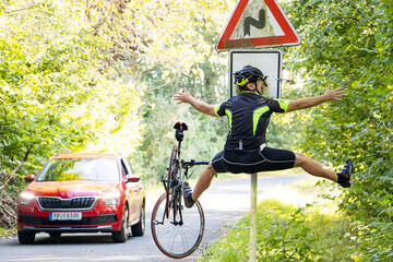 A falling cyclist bumps into a road sign next to road with traffic - obrazy, fototapety, plakaty