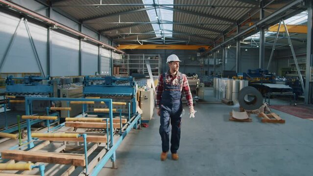 Man wearing safety uniform and hard hat walking checks production processes in factory. Look around. Inspector in warehouse.