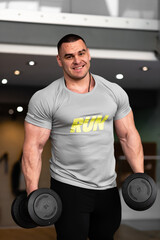 Fototapeta na wymiar A man is engaged in a gym with dumbbells, shakes the muscles of his arms and back, does exercises, a young athlete in a large gym