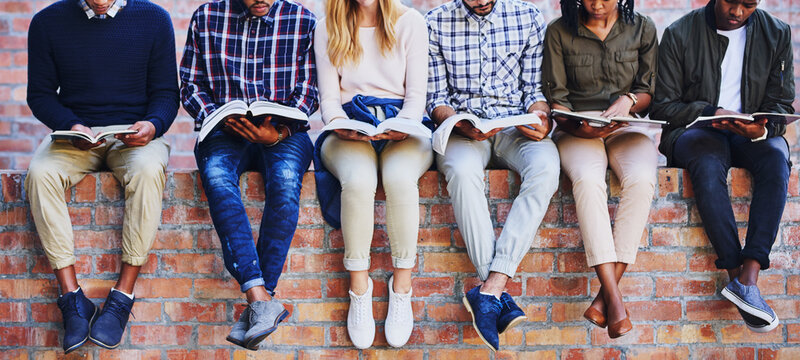 Studying on campus. Cropped shot of a group of unrecognizable university students studying while sitting outside on a facebrick wall.