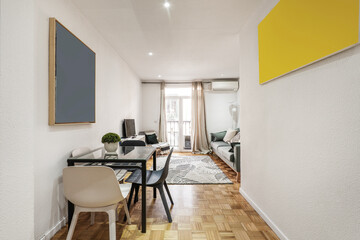 Apartment living room with square glass and metal dining table, resin chairs, white and gray rug and three-seater sofa next to a balcony with cream curtains
