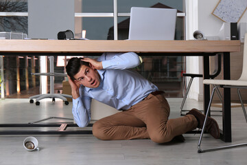 Scared man hiding under office desk during earthquake