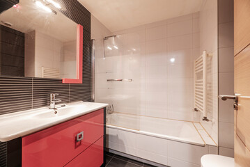 Bathroom with white porcelain sink, rectangular mirror, hanging cabinet with red wood, aluminum towel dryer and dark tiles