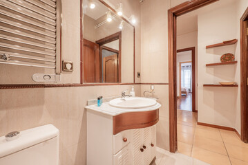 Bathroom with white porcelain sink over cabinet with white and dark wood accents, wall-mounted mirror, and chrome dryer radiator