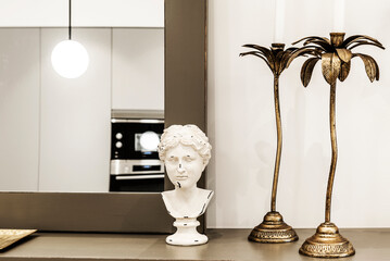sideboard with a mirror leaning against the wall, classical roman bust and gold colored metal candle holder