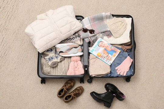 Open suitcase with warm clothes, accessories and shoes on floor, flat lay