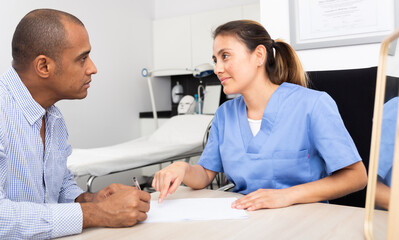 Fototapeta premium Portrait of professional colombian female cosmetologist planning upcoming treatments for male patient in modern aesthetic medicine office