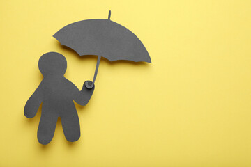 Black paper cutout of human holding umbrella on yellow background, top view with space for text....