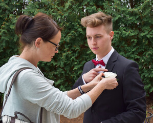 Mother attaching white rose boutonniere to her son's prom jacket